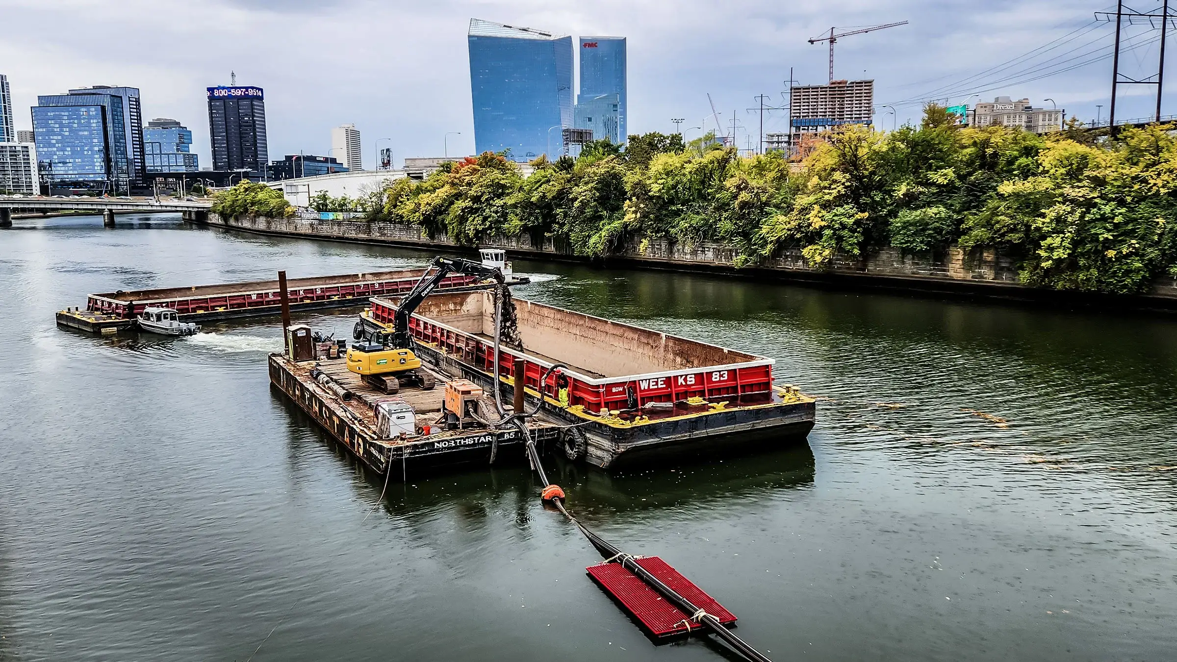 An excavator operates on a barge near several boats